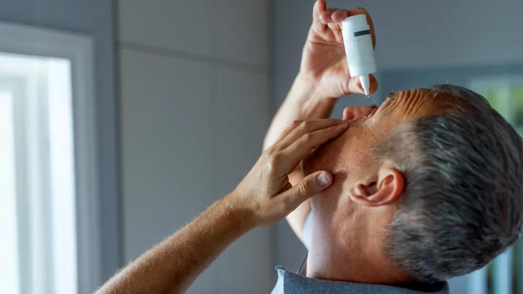 man putting eye drops in eyes 