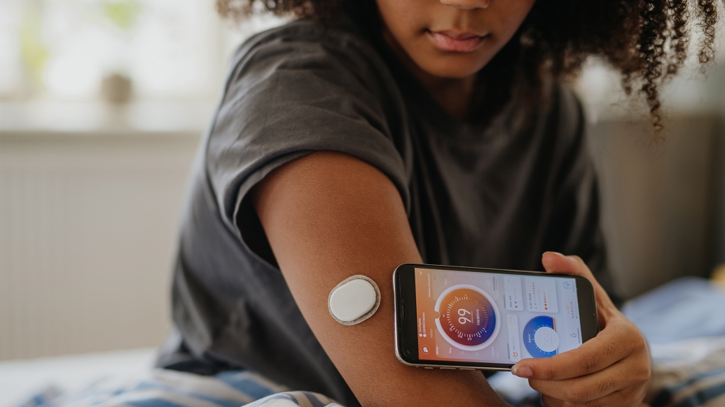 teen girl in t-shirt checking device on arm linked to phone which she holds up to her arm 