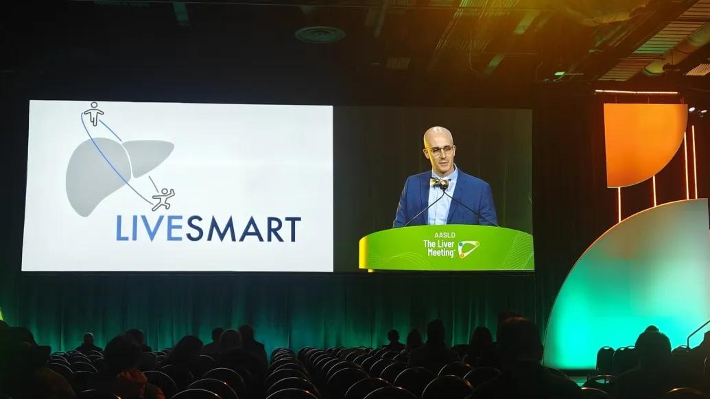 man presenting at conference with glasses dark room screen