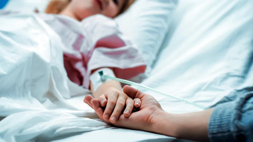 girl in hospital bed holding parents hand