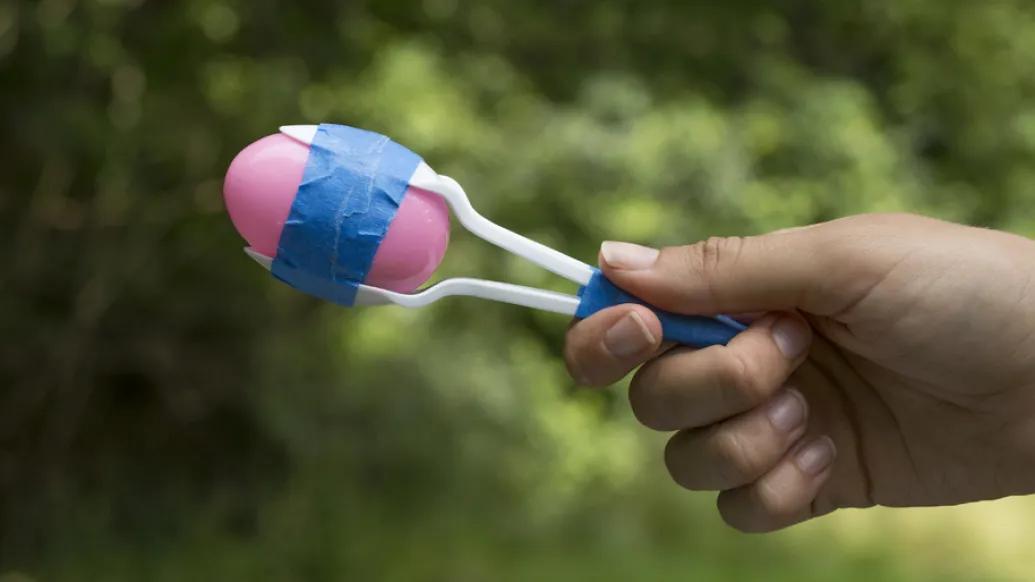 A hand holding a homemade maracas made out of plastic spoons, eggs and tape.