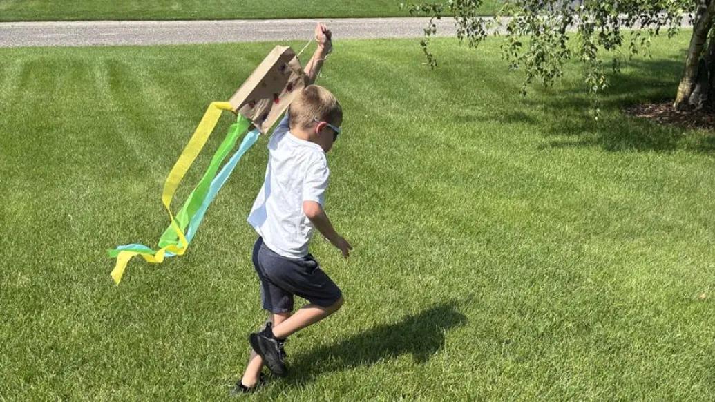 child runs with homemade kite in yard
