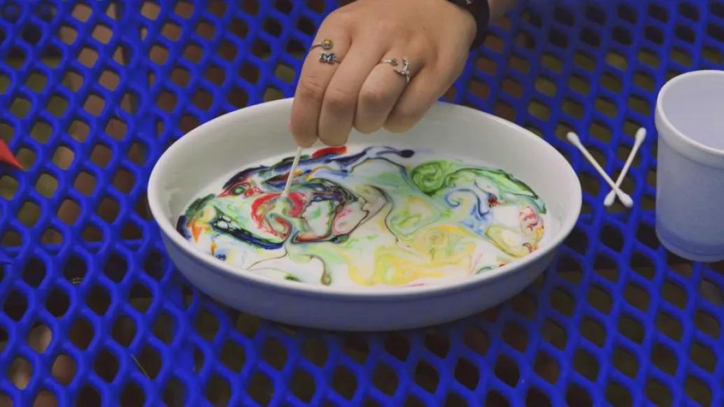 color swirls into bowl of milk on picnic table