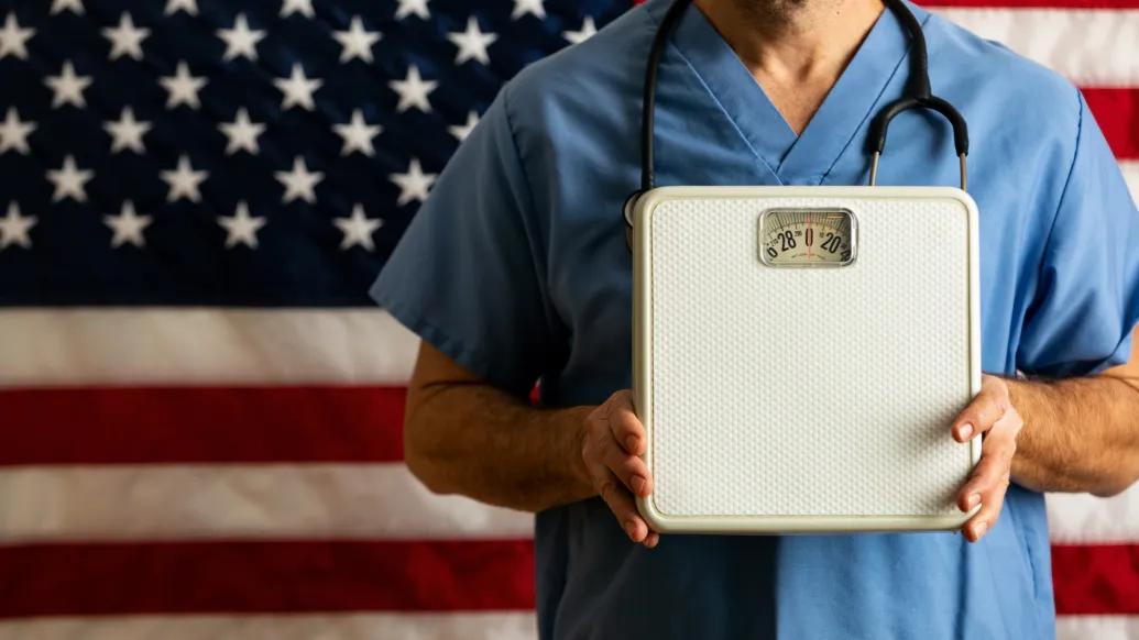 person holding scale with scrubs on and stethoscope 