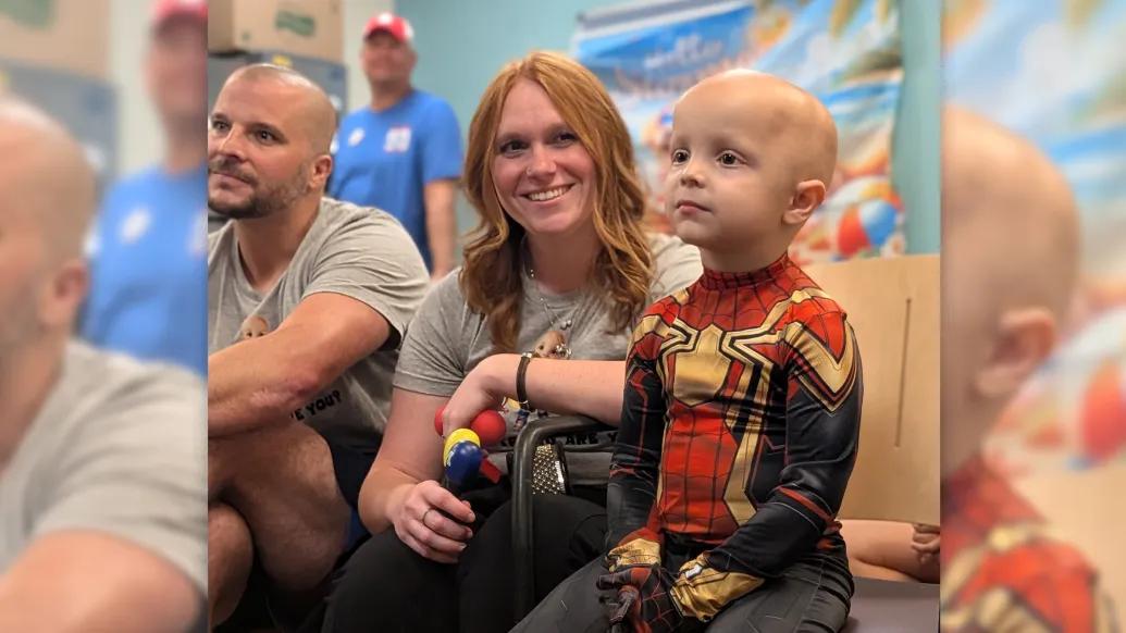 boy dressed as spiderman next to woman red hair smiling and man sitting on floor in playroom
