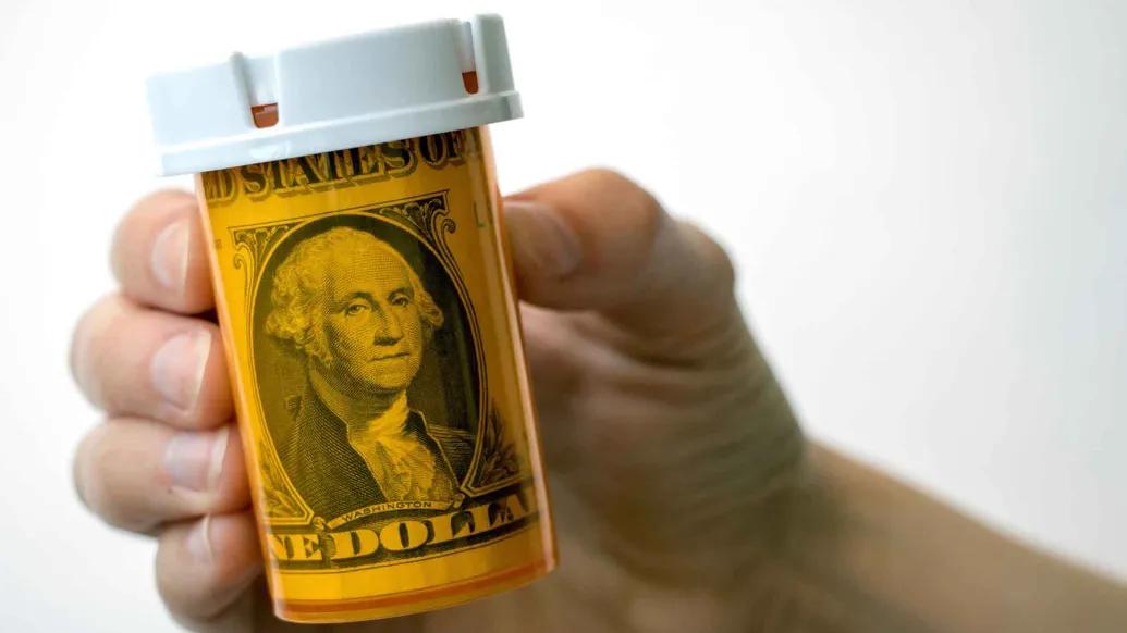 A hand holding a prescription bottle with a dollar bill in it