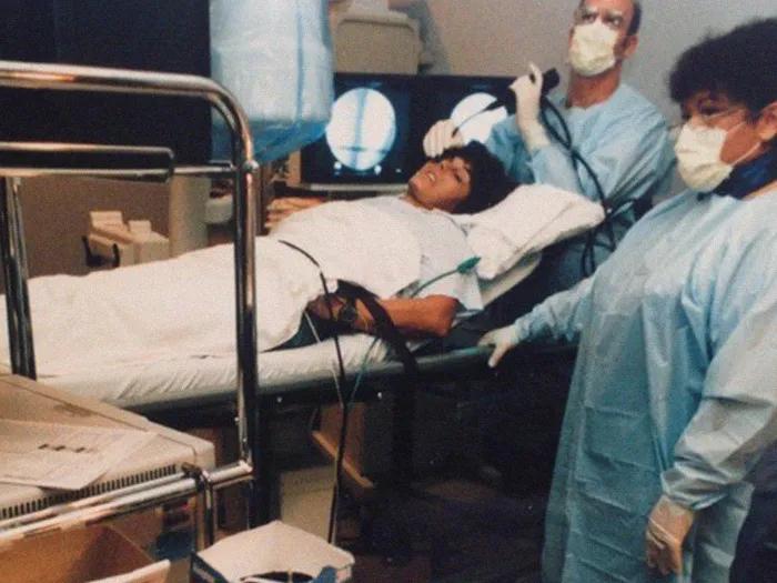 woman on hospital bed with two nurses with masks and blue gown