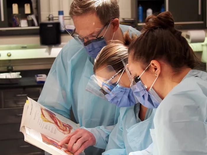 lab students and professor in gear reading textbook