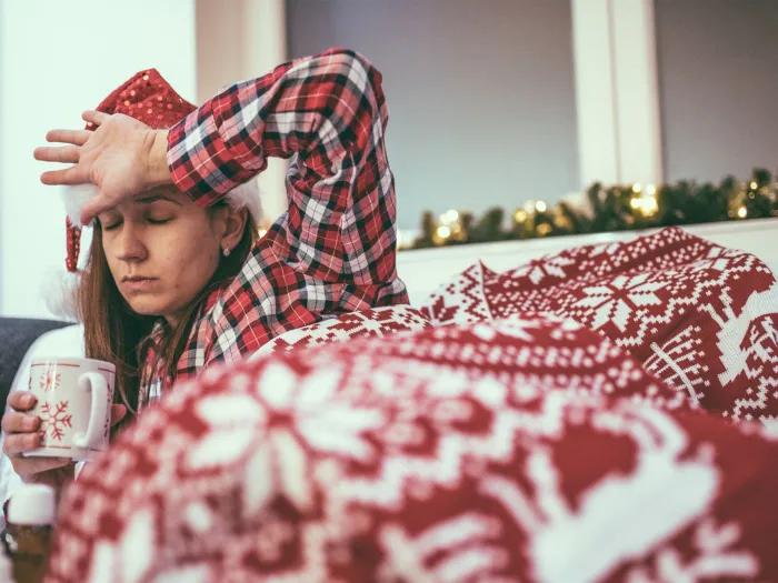 Woman covered with a red and white print blanket laying on a sofa.