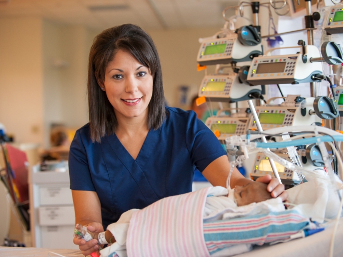 Nurse caring for an infant wrapped in blue and pink striped blankets.