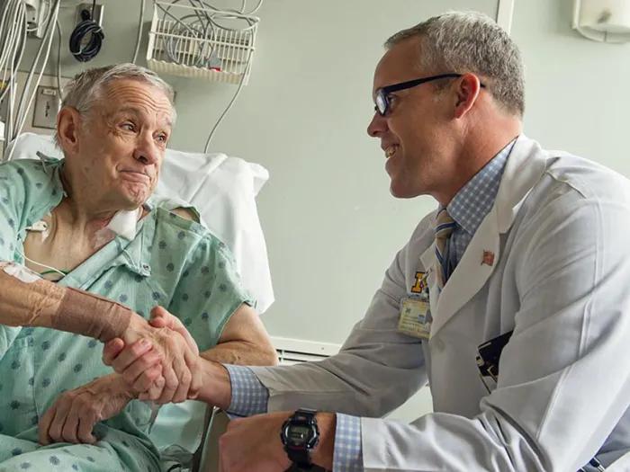 A patient and a doctor in a hospital room. They are smiling and shaking hands.