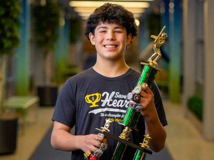teen boy smiling and posing with green gold trophy blurred background hallway