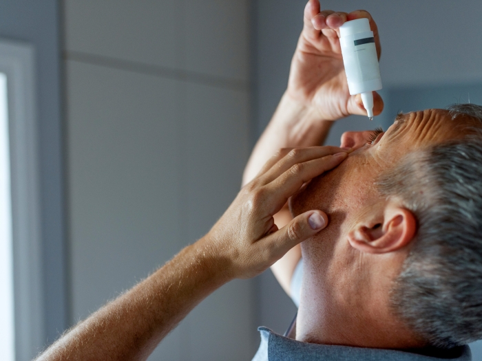 man putting eye drops in eyes 