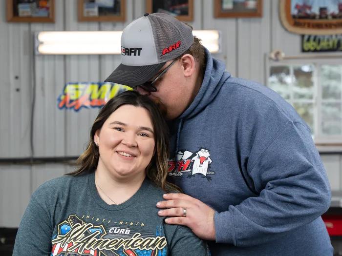 A couple-one standing and kissing the other on the top of the head.