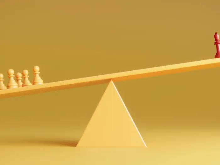 chess pieces yellow background one red piece on right and yellow on left weighing the balance beam down