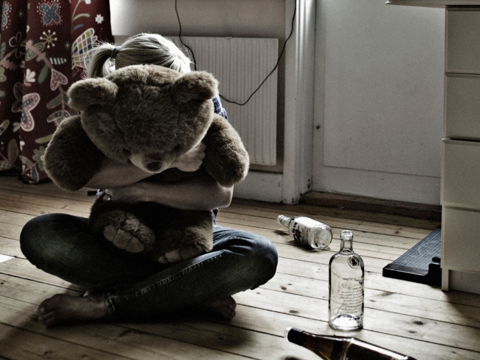 girl hugging teddy bear with alcohol bottles on ground