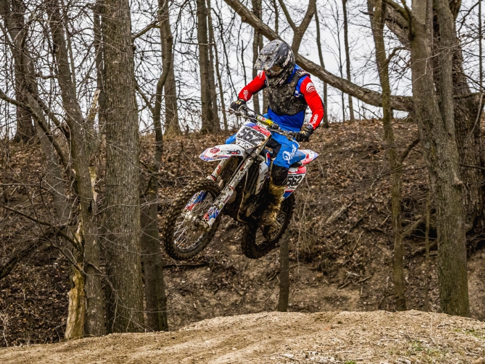 man dirt biking jumping hill in woods