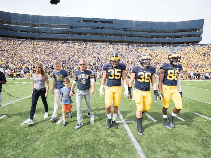 Nathan and Catherine Forbes were honorary captains during a 2015 Michigan Football game and are pictured on the field at Michigan Stadium with several players.