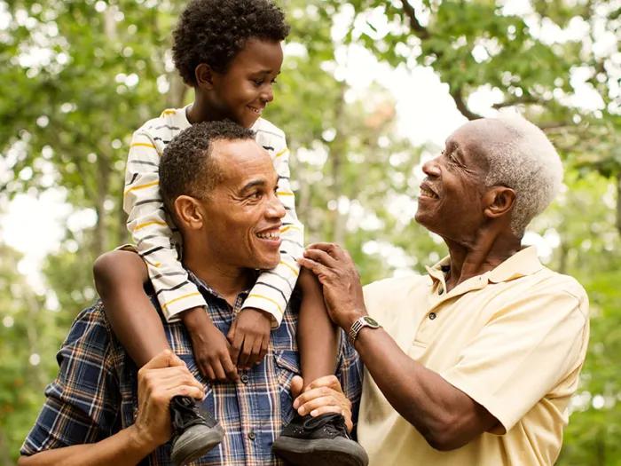 Black family with little boy on his dad's shoulders with grandpa looking on 