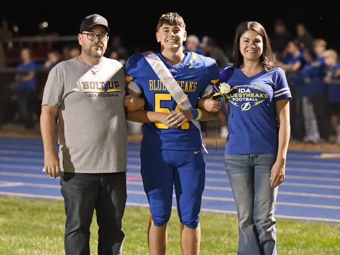 football player in middle of parents on field smiling