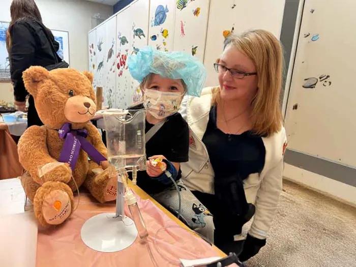 A little girl and a woman sit together with a teddy bear
