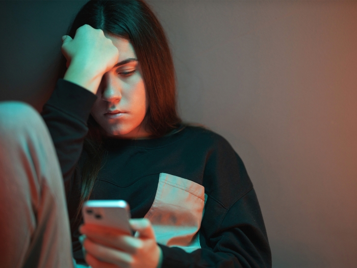 teen looking sad down at her phone dark room 
