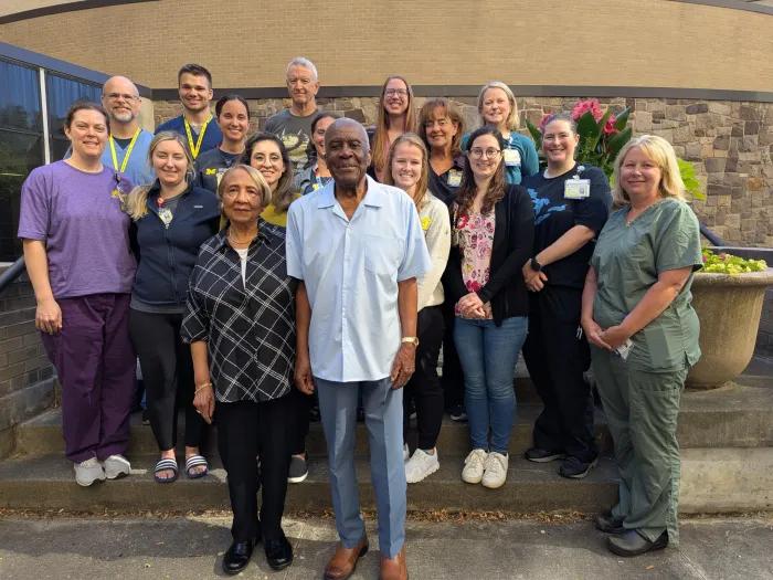 The Doziers stand next to each other smiling with 15 members of the Critical Care Unit nursing team standing in a group behind them.