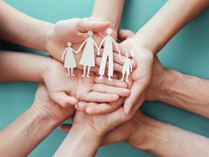 Hands coming together holding paper cut-out representing a family