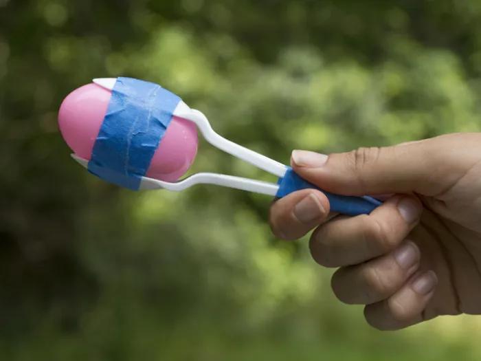 A hand holding a homemade maracas made out of plastic spoons, eggs and tape.