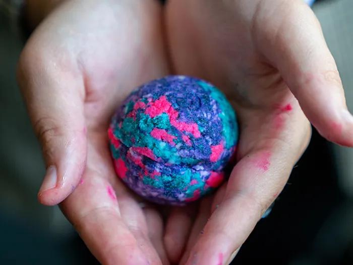 hands hold a small pink, blue and purple homemade bath bomb