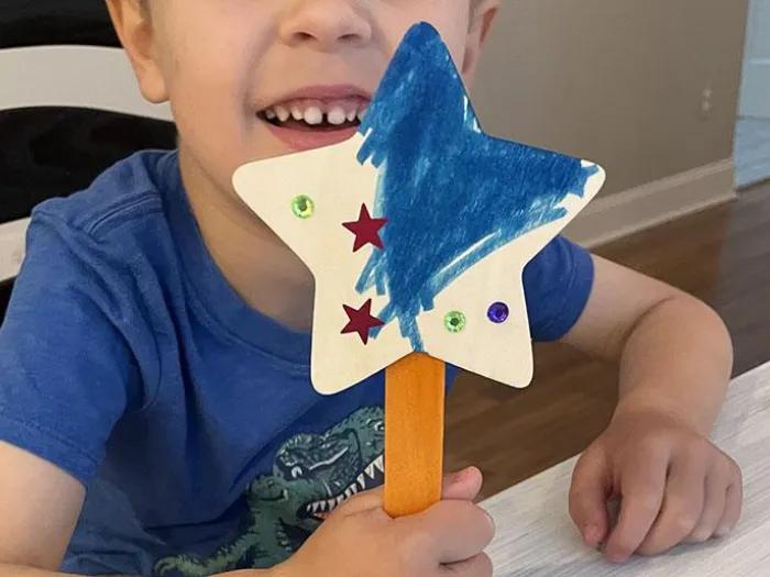 Young child holding a fairy wand they made and decorated with markers and stickers