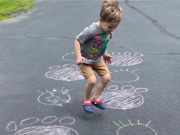 Child drawing large animal tracks on driveway with chalk