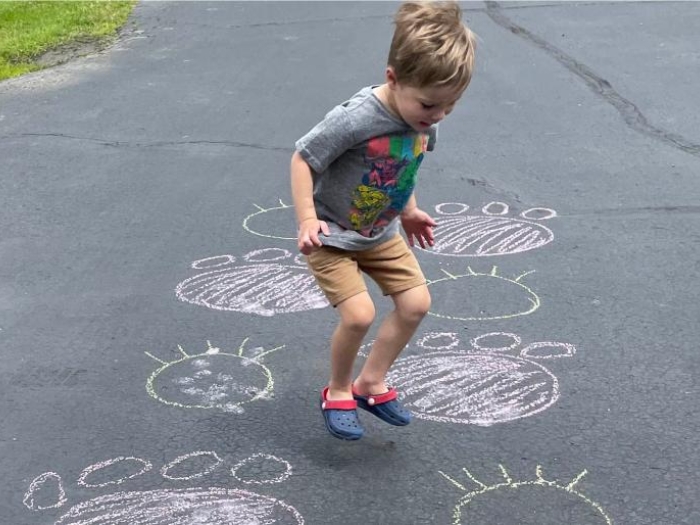 Child drawing large animal tracks on driveway with chalk