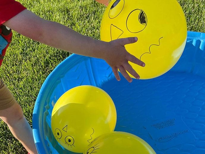 Child picking up a decorating yellow balloon from blue pool