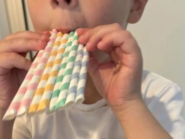 child blows through paper straw pan flute