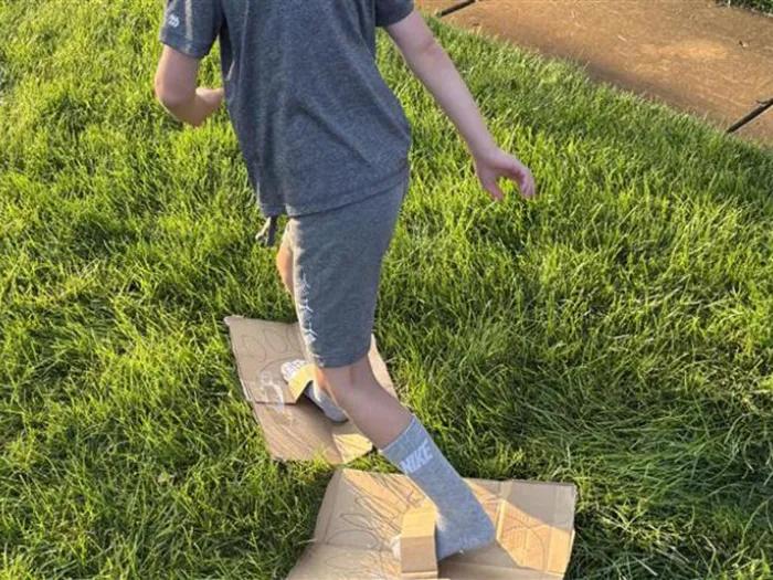 Child racing while wearing big feet made out of cardboard with taped on loops for their feet.