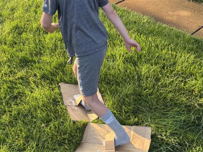 Child racing while wearing big feet made out of cardboard with taped on loops for their feet.