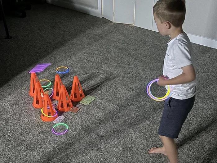 Child tossing colored rigs on orange plastic paramids