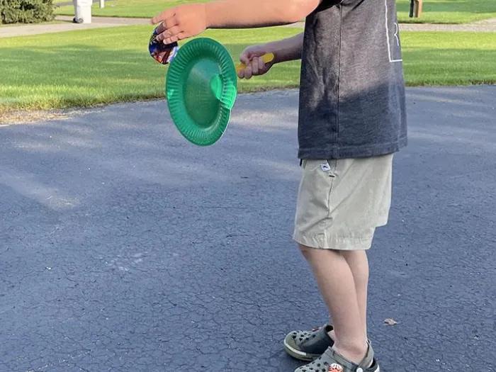 Child holding green paper plate attached to yellow popsicle stick