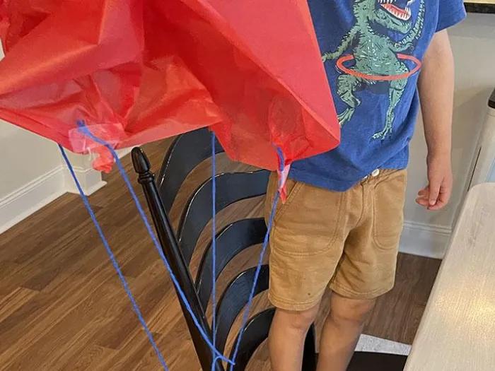 child holds handmade red toy parachute