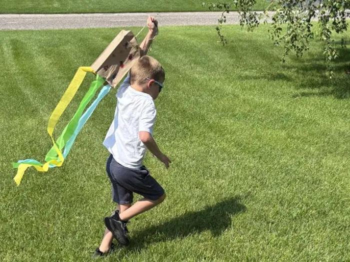 child runs with homemade kite in yard