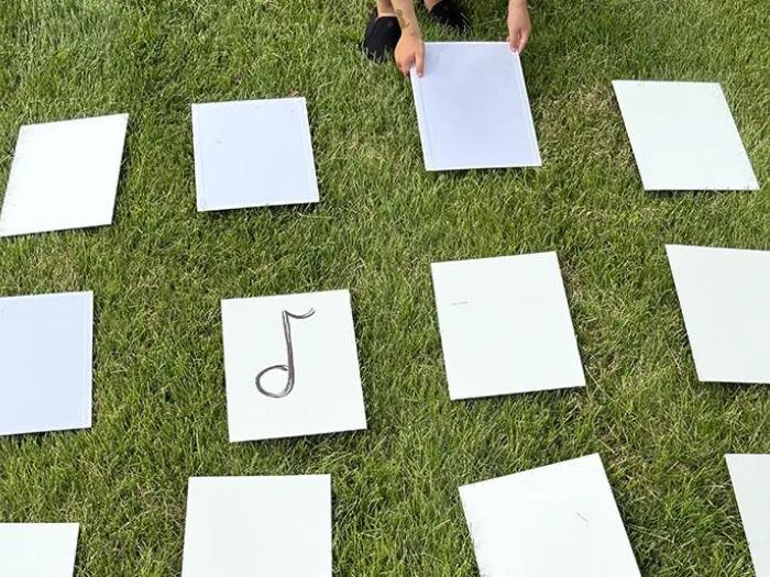 Child placing musical note cards in a row on the grass