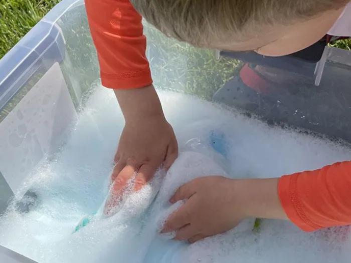 child pushes hands into "ocean foam" slime in a bucket