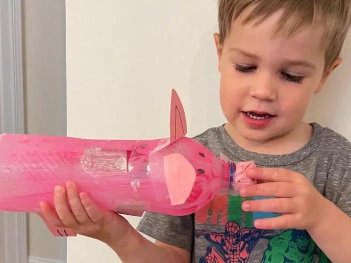 child holds pig-shaped plastic bottle piggy bank