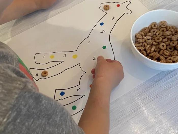 child puts cereal pieces on drawing of giraffe with colors and numbers