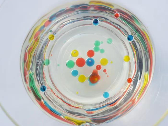 colorful oil beads collect in a glass of water