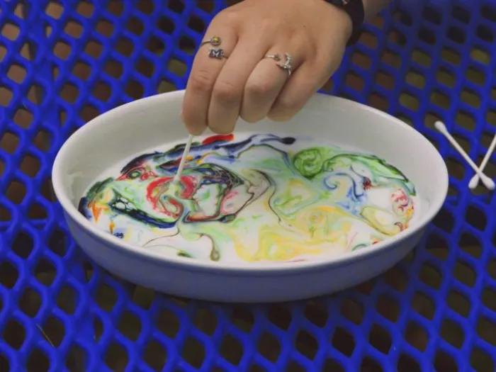 color swirls into bowl of milk on picnic table