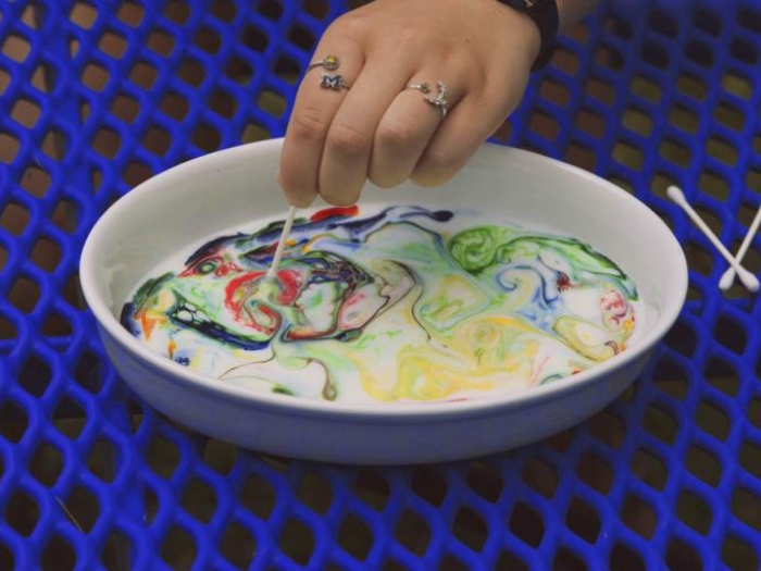 color swirls into bowl of milk on picnic table