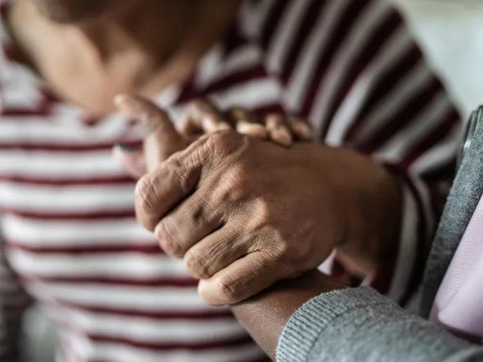 Nurse or home caregiver and senior woman holding hands at home