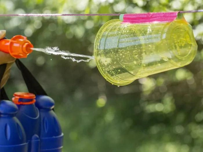 Child using squirt gun to spray plastic cup